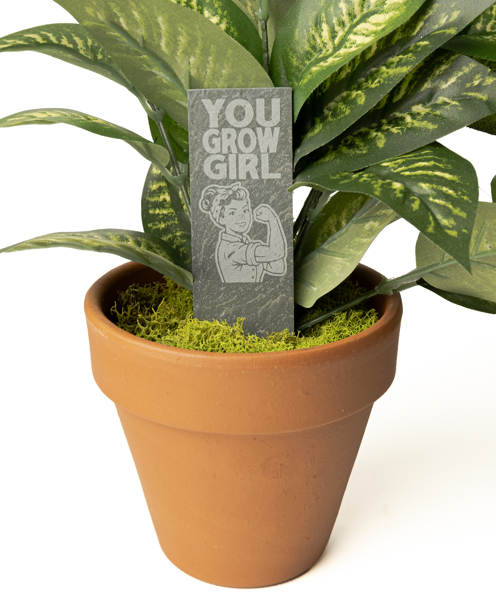 A terracotta-colored plastic pot filled with green and yellow variegated artificial plant leaves, moss, and a gray rectangular sign that reads 'YOU GROW GIRL' with a cartoon illustration.
